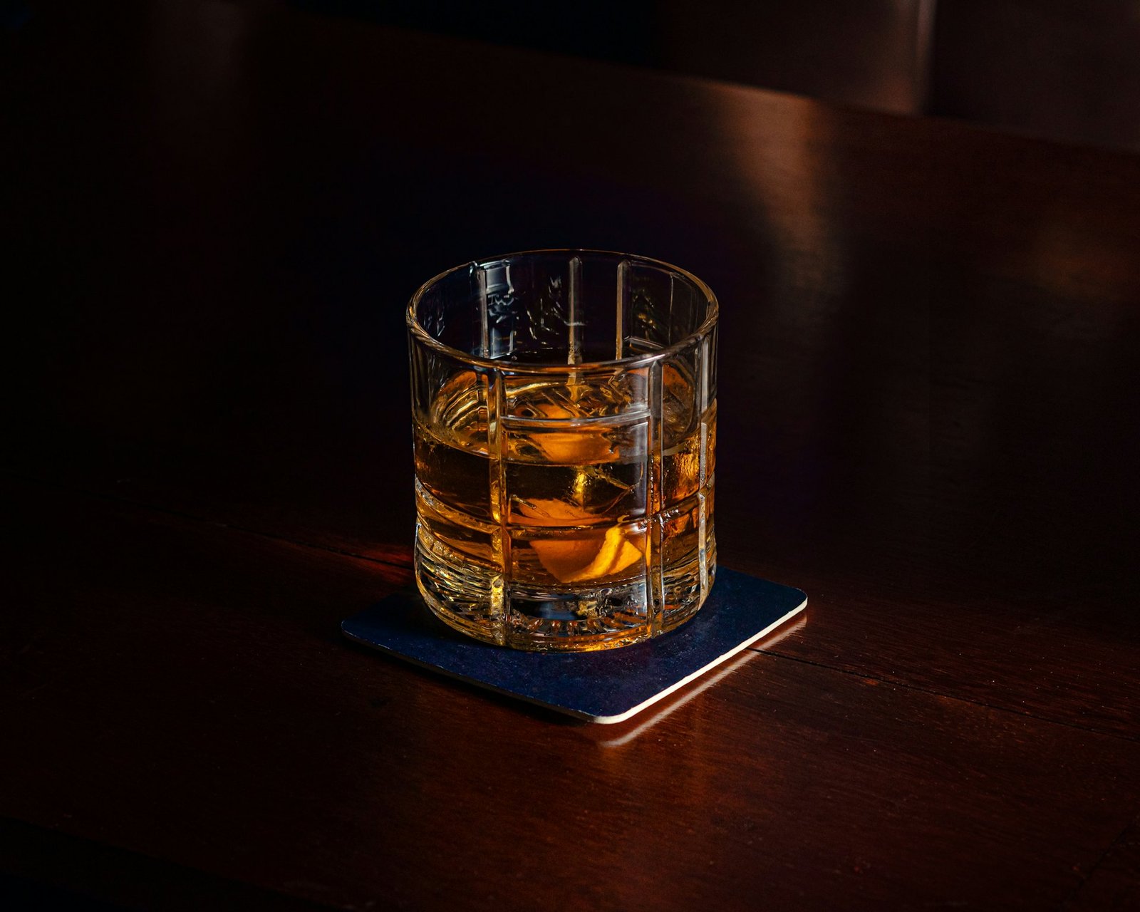 Copo de whisky sobre balcão de madeira escura